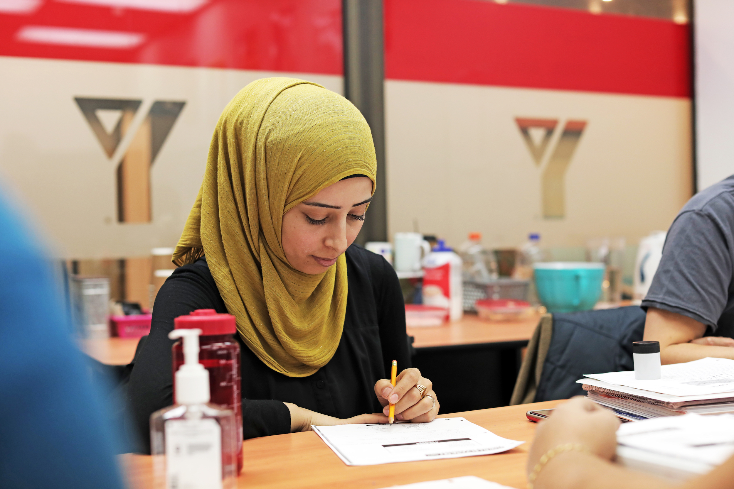 A young woman in a green hijab fills out paperwork at a YMCA facility.