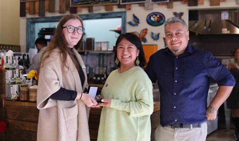 Group of three people standing together, one woman is presenting a medal to another. 